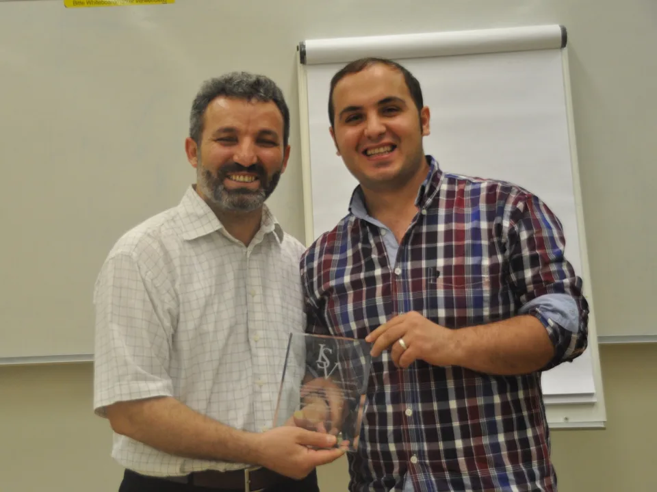 İki kişi cam bir plaketle birlikte gülümsüyor